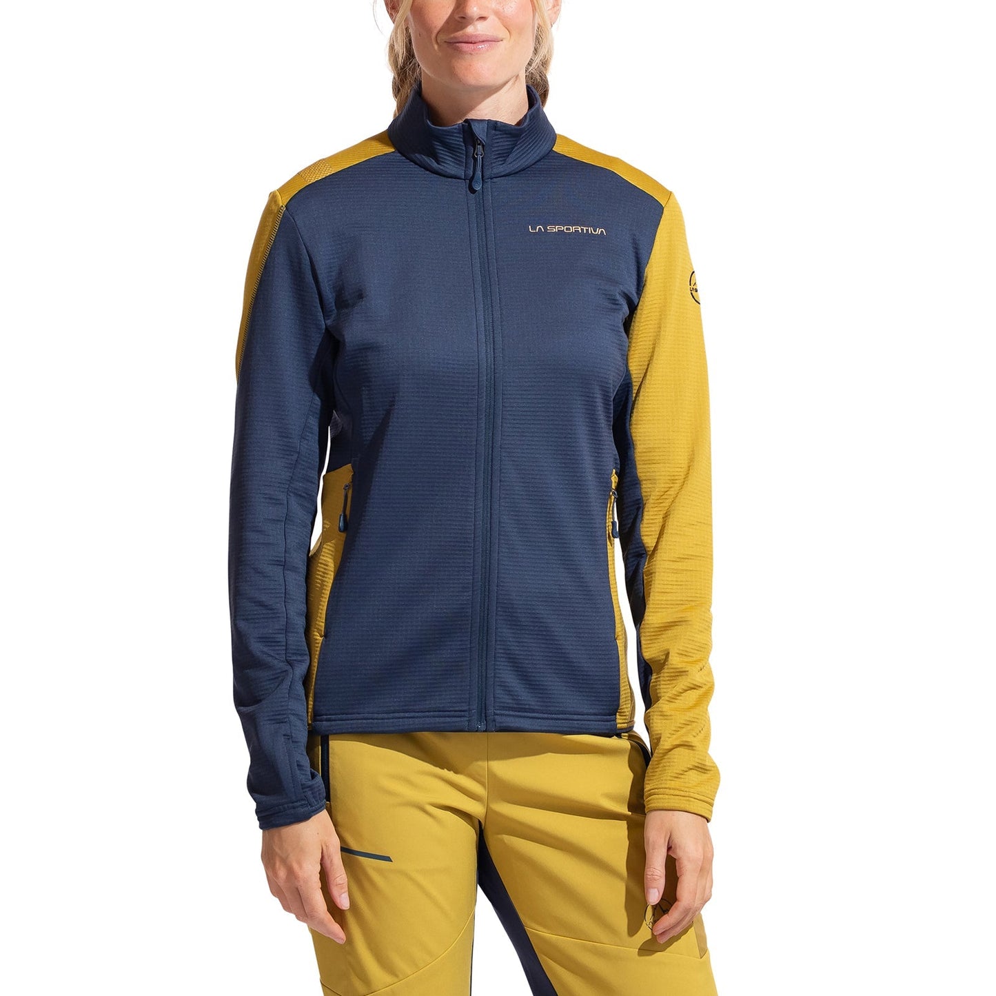 A woman wears the La Sportiva Chill Thermal Jacket Women's, featuring a dark blue front and sleeves with mustard yellow shoulders, arms, and sides. She pairs it with matching mustard yellow pants accented in blue.