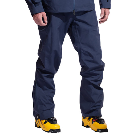 A person in La Sportiva Crest Evo Shell Pants Men's, dark blue in color, paired with bright yellow ski boots is shown from the waist down against a plain white background.