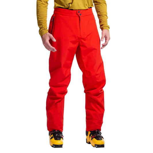 A person is shown from the shoulders down, facing forward, dressed in bright red La Sportiva Crest Evo Shell Pants, a yellow long-sleeve top, and yellow mountaineering boots.