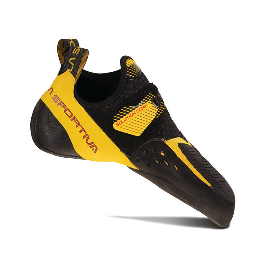 A La Sportiva Solution Comp rock climbing shoe in yellow and black, shown from the side to highlight its Velcro strap, textured rubber sole for grip, and a design optimized for toe hooks.