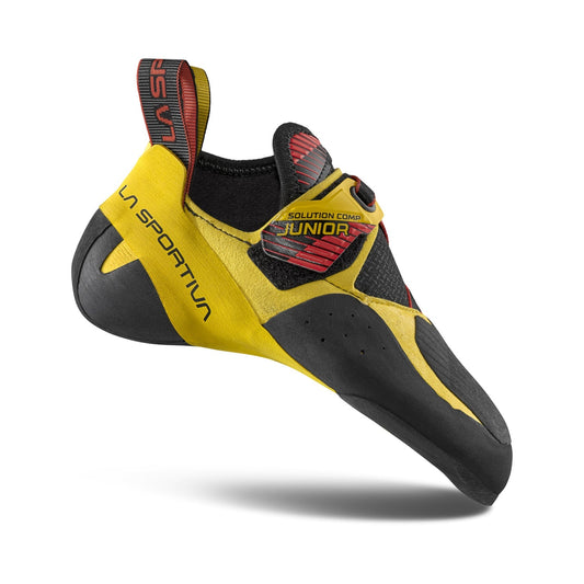 The La Sportiva Solution Comp Jr youth climbing shoe, in yellow and black with red accents, is shown side view with a heel loop for easy pull-on—designed for young climbers needing elite competition-level grip.