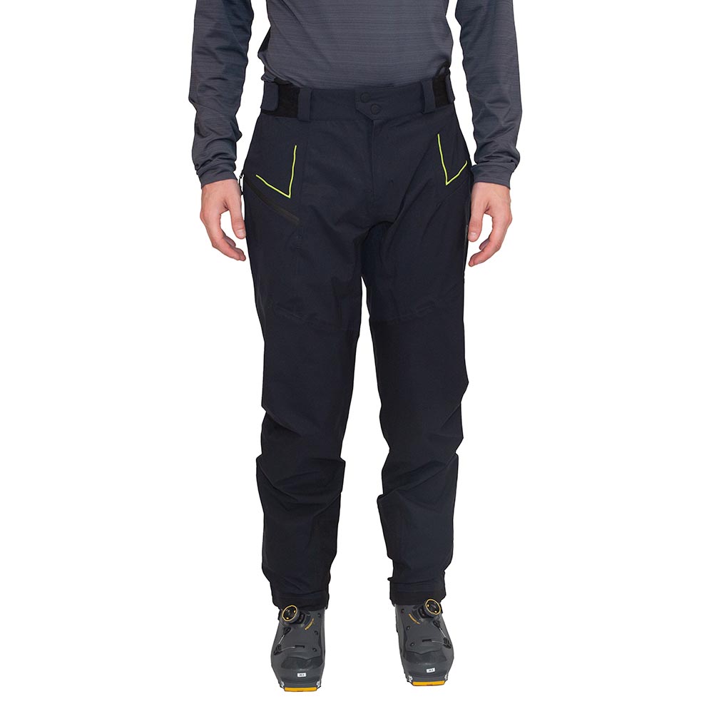 A person wearing La Sportiva Crizzle EVO Shell Pants Men’s, featuring black hardshell fabric with yellow accents, a long-sleeve dark shirt, and cycling shoes—standing facing forward against a white background.