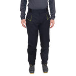 A person wearing La Sportiva Crizzle EVO Shell Pants Men’s, featuring black hardshell fabric with yellow accents, a long-sleeve dark shirt, and cycling shoes—standing facing forward against a white background.