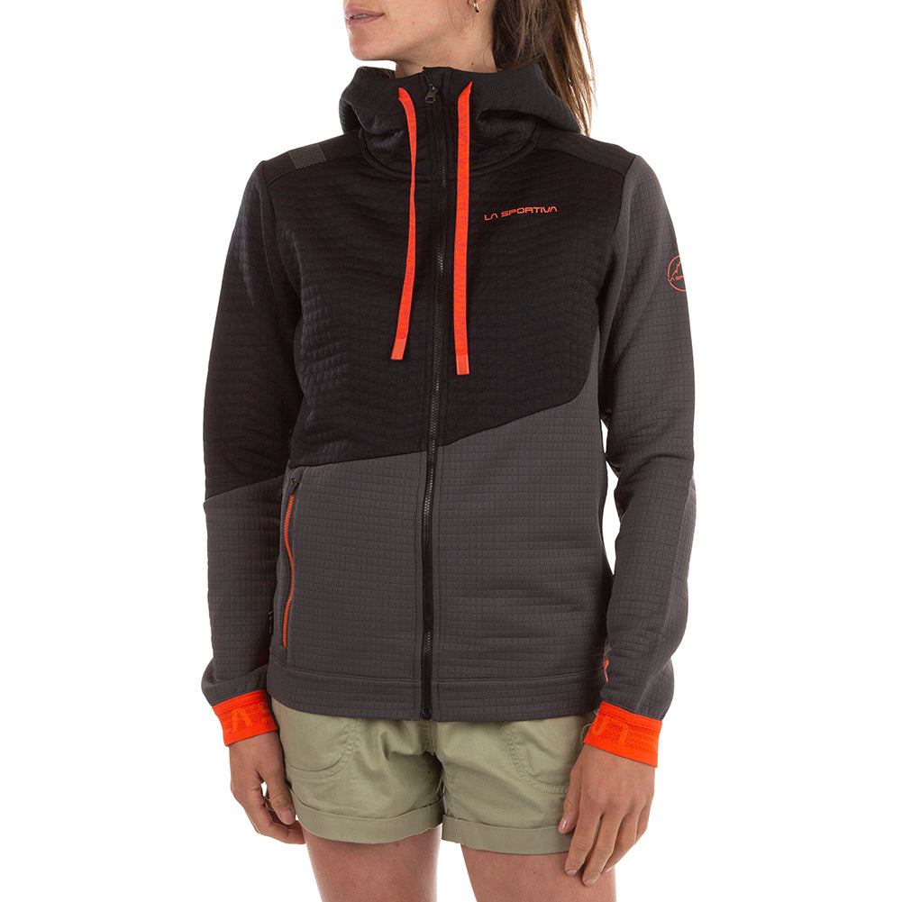 A person wearing a La Sportiva Method Hoody Women's in dark gray and black with orange accents, made from lightweight recycled fabric, paired with light green shorts, against a white background.