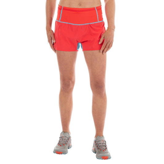 A person wears La Sportiva Vector Shorts Women's in bright red with a matching storage waistband and gray running shoes, standing facing forward. The upper body is mostly out of frame.